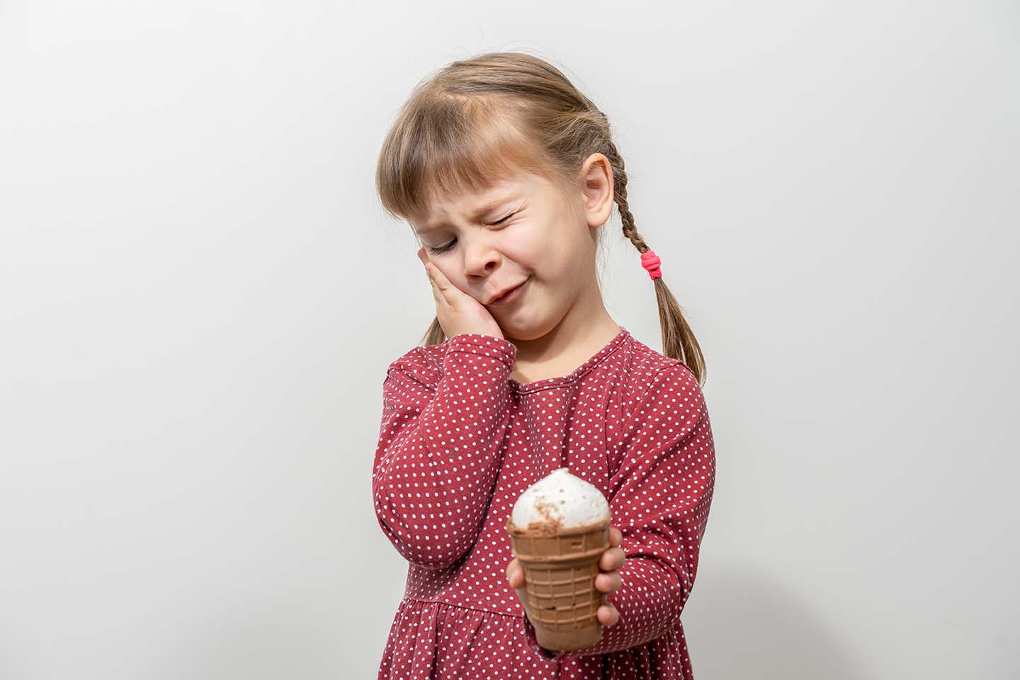 Девочка держит мороженное и касается ладонью щеки из-за зубной боли