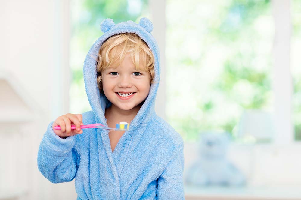 Ребенок улыбаясь держит в руках зубную щетку